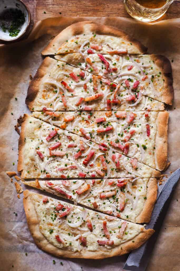 La Flammkuchen (Tarte Flambée o Pizza Alsaciana) es una pizza extra fina, crujiente, ligera y sorprendentemente rápida de hacer, ya que la masa no necesita levado (no lleva ni levadura de panadero ni química). Hoy te traigo la versión tradicional para que la tengas de base, pero cógela y juega con los ingredientes al gusto. Lo importante es que si te entra antojo de pizza y no tienes mucho tiempo, esta pizza alsaciana es la que buscas. | Receta de Paula's Apron