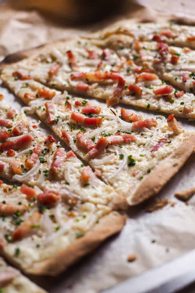 La Flammkuchen (Tarte Flambée o Pizza Alsaciana) es una pizza extra fina, crujiente, ligera y sorprendentemente rápida de hacer, ya que la masa no necesita levado (no lleva ni levadura de panadero ni química). Hoy te traigo la versión tradicional para que la tengas de base, pero cógela y juega con los ingredientes al gusto. Lo importante es que si te entra antojo de pizza y no tienes mucho tiempo, esta pizza alsaciana es la que buscas. | Receta de Paula's Apron