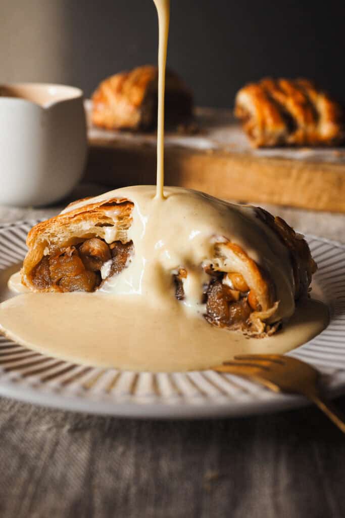 Hoy vamos con uno de esos postres fáciles y resultones que siempre te hacen quedar bien, una Trenza de Hojaldre Rellena de Manzana con Crema Inglesa. El hojaldre va relleno con manzana ligeramente pochada (para que no quede dura en el poco tiempo de horno que necesita la trenza) y avellanas para un toque crujiente dentro del mismo relleno. Lo podríamos dejar aquí, pero hoy como acompañamiento, para variar del típico helado, crema inglesa. Su aroma a vainilla y untuosidad no le pueden ir mejor ni al hojaldre ni a la manzana, y ya verás que es cero complicada. Es un postre que puedes preparar con antelación y todo junto hace un combo espectacular. | Receta de Paula's Apron