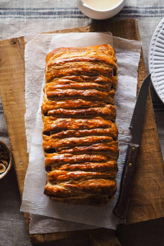 Hoy vamos con uno de esos postres fáciles y resultones que siempre te hacen quedar bien, una Trenza de Hojaldre Rellena de Manzana con Crema Inglesa. El hojaldre va relleno con manzana ligeramente pochada (para que no quede dura en el poco tiempo de horno que necesita la trenza) y avellanas para un toque crujiente dentro del mismo relleno. Es un postre que puedes preparar con antelación y todo junto hace un combo espectacular. | Receta de Paula's Apron