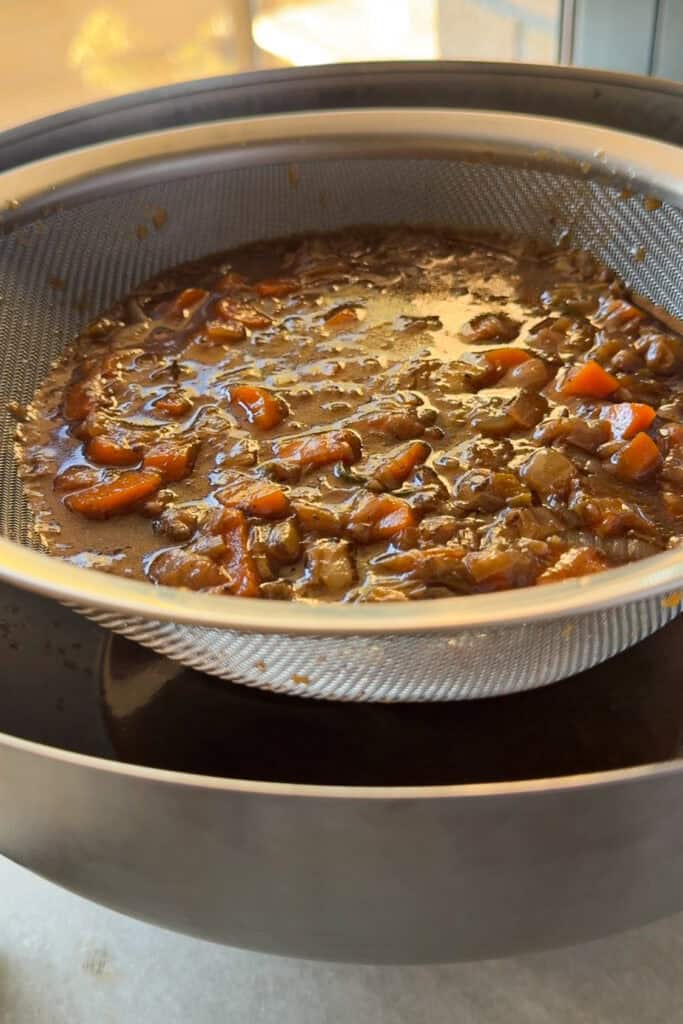 Caldo de hacer carrilleras colado con las verduras en un colador.