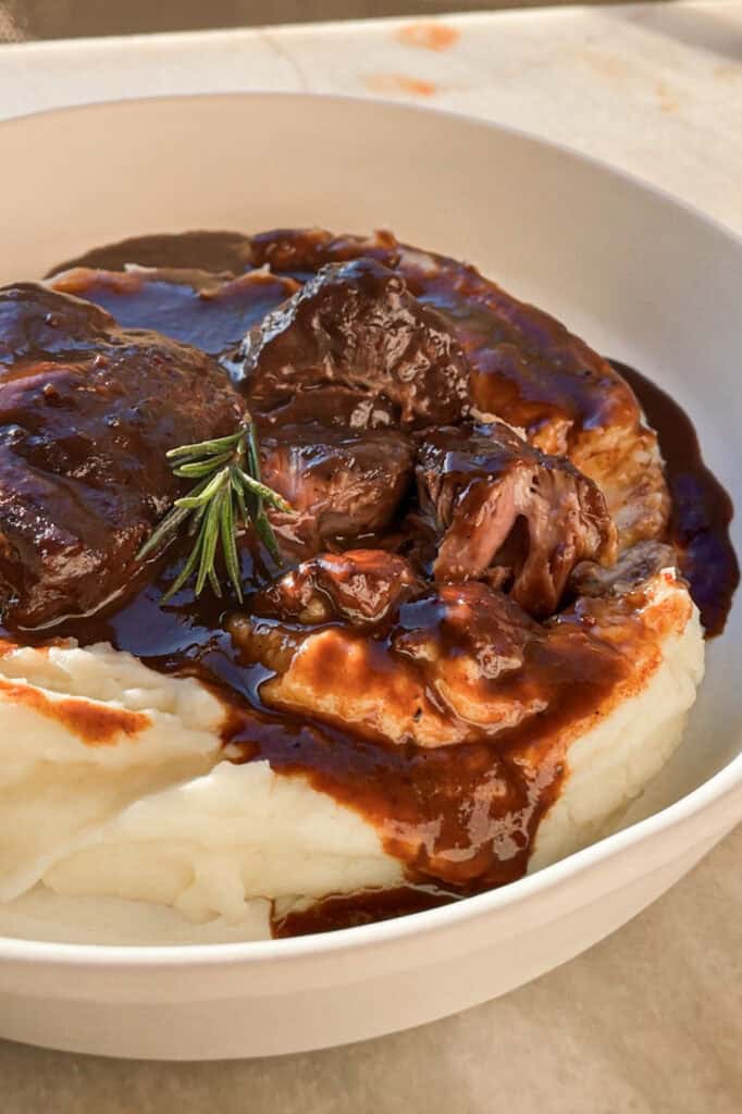 Mis recetas favoritas son sin duda las recetas tradicionales como esta, unas Carrilleras al Vino Tinto que te quitan el sentido y que harían orgullosa a mi abuela. Quedan melosas, tiernas y la salsa es de esas para mojar todo el pan del mundo, porque no querrás dejar ni una gota. Como buen guiso, requiere cariño y paciencia, pero con 4 pasos lo tienes, no pide más. Acompáñalas de puré de chirivía para una opción ligera, de polenta cremosa o el clásico puré de patatas y a desmayarte de placer cuando les pegues un bocado. | Receta de Paula's Apron