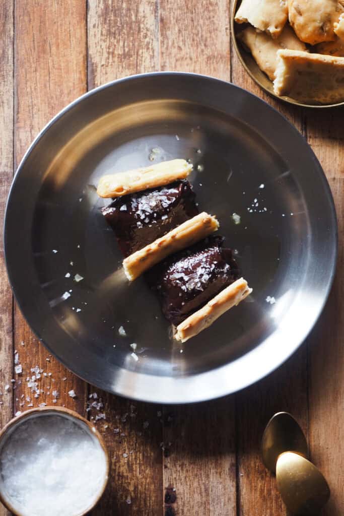 ¿Puede que sea el postre de chocolate más fácil del mundo? Puede, pero esta versión del clásico pan con chocolate, aceite y sal nunca deja a nadie indiferente. El chocolate queda suave, nada pesado, y le he dado un toque de naranja aprovechando que está de temporada pero puedes aromatizarlo como quieras o dejarlo tal cual (luego te dejo opciones). Para rematar, toque salado con sal marina en escamas, un buen aceite de oliva virgen extra y en lugar de unas tostadas típicas a mi me gusta acompañarlo con pan de pipas, que siempre siempre siempre sorprende. | Receta de Paula's Apron