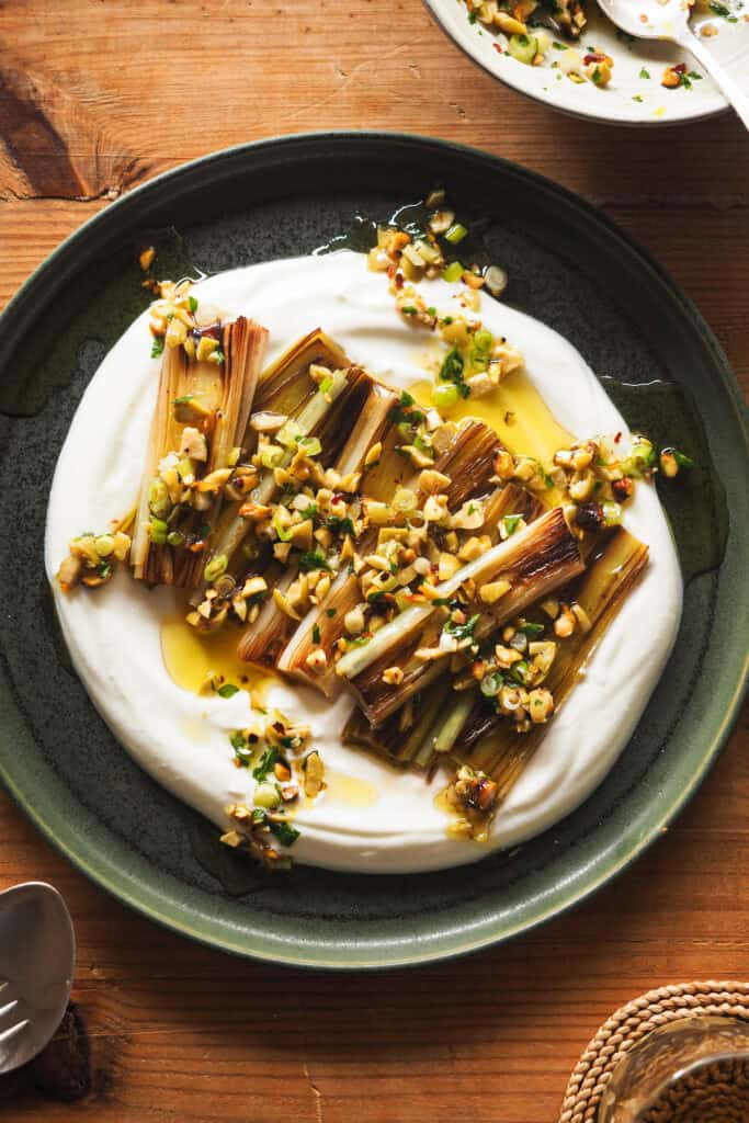 Nueva idea para demostrarte que el puerro puede ser un protagonista increíble: Puerros Caramelizados con Aliño de Aceitunas y Pistachos. Hoy vamos a aprender una técnica alternativa a asarlos para también conseguir un puerro suave, dulzón y con una textura que se deshace en boca. Sólo necesitas 15 minutos más o menos y vamos a aprovechar el rato de cocción para preparar un topping y una base que van a llevar esta receta de un acompañamiento delicioso a un entrante espectacular. | Receta de Paula's Apron