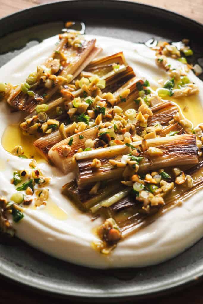 Nueva idea para demostrarte que el puerro puede ser un protagonista increíble: Puerros Caramelizados con Aliño de Aceitunas y Pistachos. Hoy vamos a aprender una técnica alternativa a asarlos para también conseguir un puerro suave, dulzón y con una textura que se deshace en boca. Sólo necesitas 15 minutos más o menos y vamos a aprovechar el rato de cocción para preparar un topping y una base que van a llevar esta receta de un acompañamiento delicioso a un entrante espectacular. | Receta de Paula's Apron