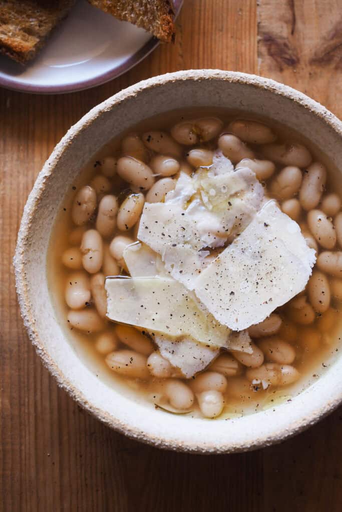 Cómo cocer alubias es algo que todos deberíamos saber hacer. Además de rebote te sale un caldo sabroso, nutritivo, fácil y versátil que puedes usar de mil formas, así como las alubias cocidas resultantes. Las alubias secas son mucho más económicas que comprarlas en bote, puedes hacer en cantidad y conservarlas para usarlas en una infinidad de platos, como esta sopa de alubias y parmesano. | Receta de Paula's Apron