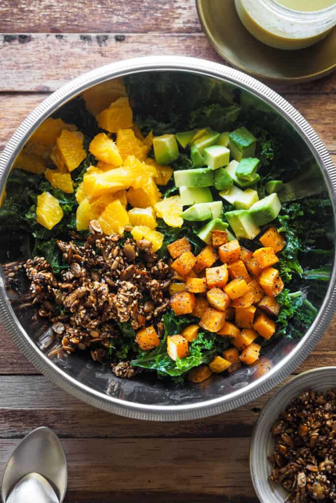 El invierno también es para ensaladas y se pueden hacer coloridas, nutritivas, sabrosas y deliciosas como esta Ensalada de Kale con Calabaza y Crujiente de Semillas. Además lleva naranja, que también está de temporada y que le aporta textura, sabor y un extra de nutrientes y fibra, y aguacate que aporta untuosidad al mezclarse con el resto. El aliño además es igual de especial, ligeramente ácido y cremoso para conseguir que el kale pierda su textura algo correosa. Bonus: todos los elementos que requieren algo de elaboración se pueden usar de muchas otras maneras, por lo que puedes hacer en más cantidad y usarlos otras veces. | Receta de Paula's Apron