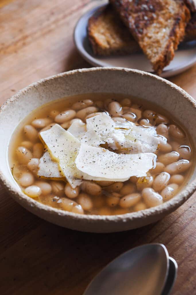 Cómo cocer alubias es algo que todos deberíamos saber hacer. Además de rebote te sale un caldo sabroso, nutritivo, fácil y versátil que puedes usar de mil formas, así como las alubias cocidas resultantes. Las alubias secas son mucho más económicas que comprarlas en bote, puedes hacer en cantidad y conservarlas para usarlas en una infinidad de platos, como esta sopa de alubias y parmesano. | Receta de Paula's Apron