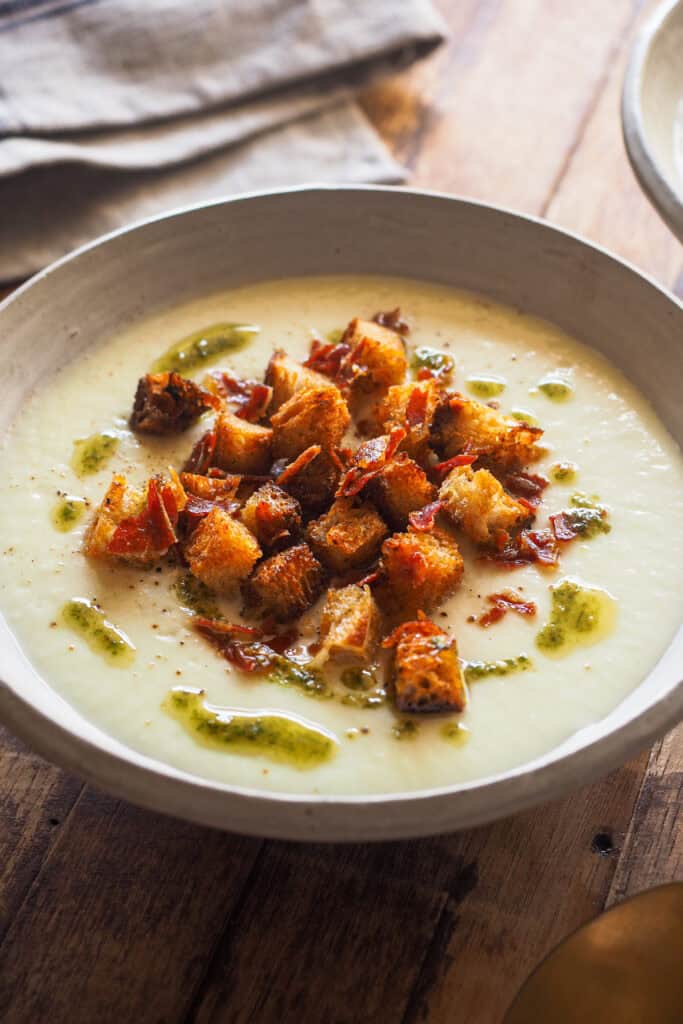 Hoy, en un nuevo episodio convirtiendo verduras humildes y relegadas a un solo uso en protagonistas: Crema de Chirivía y Nabo con Queso Manchego. Tanto el nabo como la chirivía son verduras que solemos usar solo para enriquecer caldos, pero se puede hacer magia con ellos y te lo voy a demostrar con esta crema sencilla y rápida de preparar, pero llena de sabor y con una textura extra cremosa gracias a estas verduras. Para acompañarla, unos picatostes clásicos pero con toque de pimentón (para contrastar de color y sabor), jamón serrano crujiente y salino para contrastar con el dulzor natural de la crema y pesto, que lo redondea y equilibra todo. | Receta de Paula's Apron