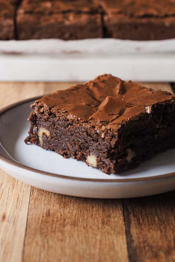 ¿En busca del brownie de chocolate perfecto? Después de semanas desarrollando esta receta, al fin te traigo la que para mi es la receta de brownie casero ideal. Tierno, pero sin ser abizcochado, húmedo y jugoso, pero ligero y suave a la vez, cero mazacote y con el punto de chocolate equilibrado para que no sea empalagoso. ¡Ah! Y con esa superficie brillante y quebradiza, ligeramente crujiente, que contrasta con la textura del interior, una mezcla perfecta entre "chewy" y "fudgy". Como toque final, y opcional, la cantidad justa de nueces para encontrarte un trocito aquí y allí pero sin que manden. ¡Ha sido la versión favorita entre todos mis amigos y familia, así que espero que te encante! | Receta de Paula's Apron