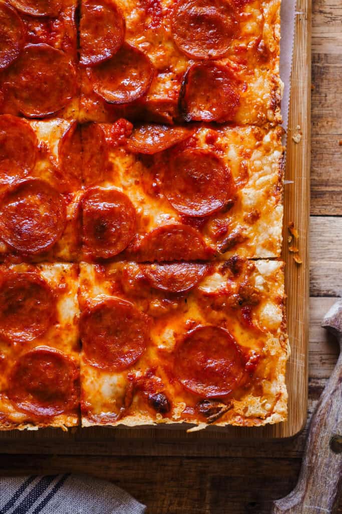 Estoy de vuelta una vez más con pizzas por el mundo, porque existen un montón de tipos de pizza increíbles como la Pizza Estilo Detroit que te traigo hoy y encima con una masa que no necesita amasado. Imagínate una base suave, ligera y esponjosa, parecida a la de la focaccia, una costra de queso por todo el perímetro y el topping que más te guste, ¿suena bien no? Hoy en concreto voy a usar el topping típico de la "Detroit-Style Pizza" con queso, salsa de tomate y pepperoni. ¡Ah! Y no te extrañes por el orden en que los pongo, es algo que caracteriza a este tipo de pizza. | Receta de Paula's Apron