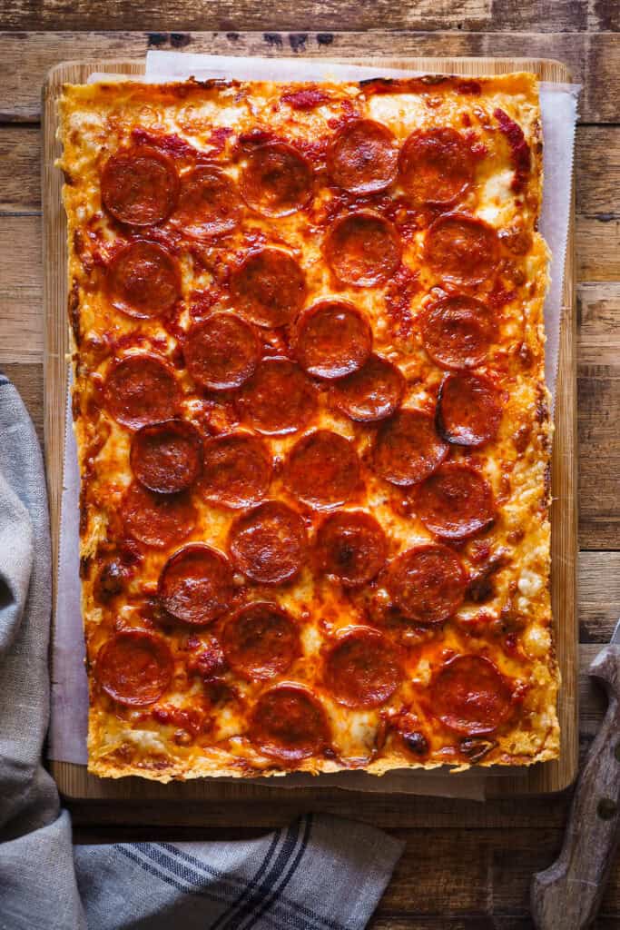 Estoy de vuelta una vez más con pizzas por el mundo, porque existen un montón de tipos de pizza increíbles como la Pizza Estilo Detroit que te traigo hoy y encima con una masa que no necesita amasado. Imagínate una base suave, ligera y esponjosa, parecida a la de la focaccia, una costra de queso por todo el perímetro y el topping que más te guste, ¿suena bien no? Hoy en concreto voy a usar el topping típico de la "Detroit-Style Pizza" con queso, salsa de tomate y pepperoni. ¡Ah! Y no te extrañes por el orden en que los pongo, es algo que caracteriza a este tipo de pizza. | Receta de Paula's Apron