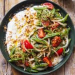 Esta Ensalada de Judías Verdes y Tomate con Dukkah es una versión reinventada de un clásico de mi infancia. No sé tu, pero yo he crecido comiendo ensalada de judías verdes, tomate y cebolla con atún (y a veces huevo duro) cada verano de mi vida, semana sí semana también XD. Hoy mantengo las hortalizas y la vinagreta de mostaza que siempre hacía mi abuela para aliñarla, un combo sencillo, pero perfecto. Y le añado un toque crujiente con Dukkah casero, que además le aporta un punto aromático, junto con una base de yogur que lo redondea todo con su cremosidad y ligera acidez. En resumen, una ensalada fresquita perfecta para esta temporada. | Receta de Paula's Apron