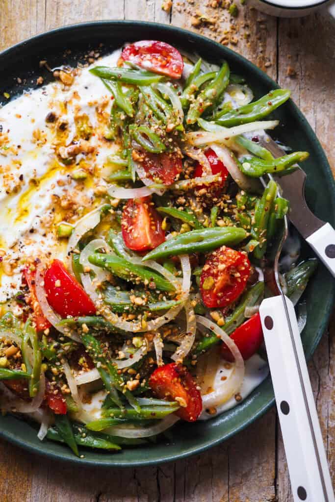 Esta Ensalada de Judías Verdes y Tomate con Dukkah es una versión reinventada de un clásico de mi infancia. No sé tu, pero yo he crecido comiendo ensalada de judías verdes, tomate y cebolla con atún (y a veces huevo duro) cada verano de mi vida, semana sí semana también XD. Hoy mantengo las hortalizas y la vinagreta de mostaza que siempre hacía mi abuela para aliñarla, un combo sencillo, pero perfecto. Y le añado un toque crujiente con Dukkah casero, que además le aporta un punto aromático, junto con una base de yogur que lo redondea todo con su cremosidad y ligera acidez. En resumen, una ensalada fresquita perfecta para esta temporada. | Receta de Paula's Apron