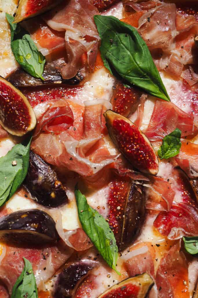 Esta versión de Flammkuchen de Higos y Jamón (Tarte Flambée de Higos y Jamón) es perfecta para finales de verano, cuando da menos pereza encender el horno y los higos están de temporada. Lleva queso y jamón para aportar contraste de color y ese equilibrio perfecto entre dulce y salado. El resultado es una pizza fina, crujiente, ligera y muy sabrosa que siempre deja a todo el mundo queriendo repetir. | Receta de Paula's Apron