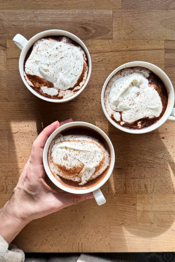 Una buena receta de chocolate caliente es un básico invernal si me preguntan. La mía es sencilla, pero cuidando el producto y los detalles para conseguir un chocolate cremoso, equilibrado y con sabor a chocolate de verdad, sin resultar pesado ni empalagoso. Además, es una receta muy versátil, perfecta para adaptar a tu gusto aromatizándola con especias, cítricos o infusiones, y convertirla en ese pequeño ritual que apetece repetir cuando refresca o simplemente cuando el cuerpo pide algo reconfortante. | Receta de Paula's Apron
