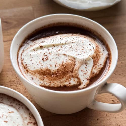 Una buena receta de chocolate caliente es un básico invernal si me preguntan. La mía es sencilla, pero cuidando el producto y los detalles para conseguir un chocolate cremoso, equilibrado y con sabor a chocolate de verdad, sin resultar pesado ni empalagoso. Además, es una receta muy versátil, perfecta para adaptar a tu gusto aromatizándola con especias, cítricos o infusiones, y convertirla en ese pequeño ritual que apetece repetir cuando refresca o simplemente cuando el cuerpo pide algo reconfortante. | Receta de Paula's Apron