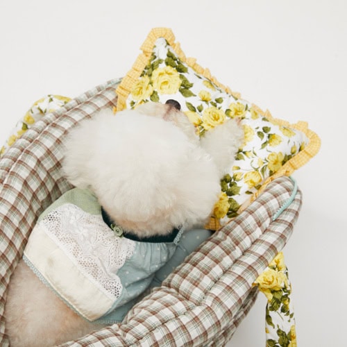 Cute white puppy resting on a floral pillow in a cozy checkered basket, showcasing pet comfort and stylish accessories for dogs.