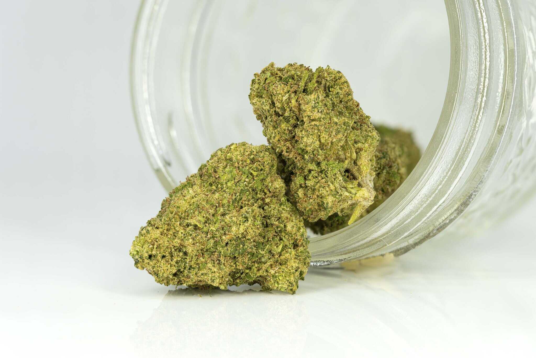 Cannabis buds spilling from a clear jar.