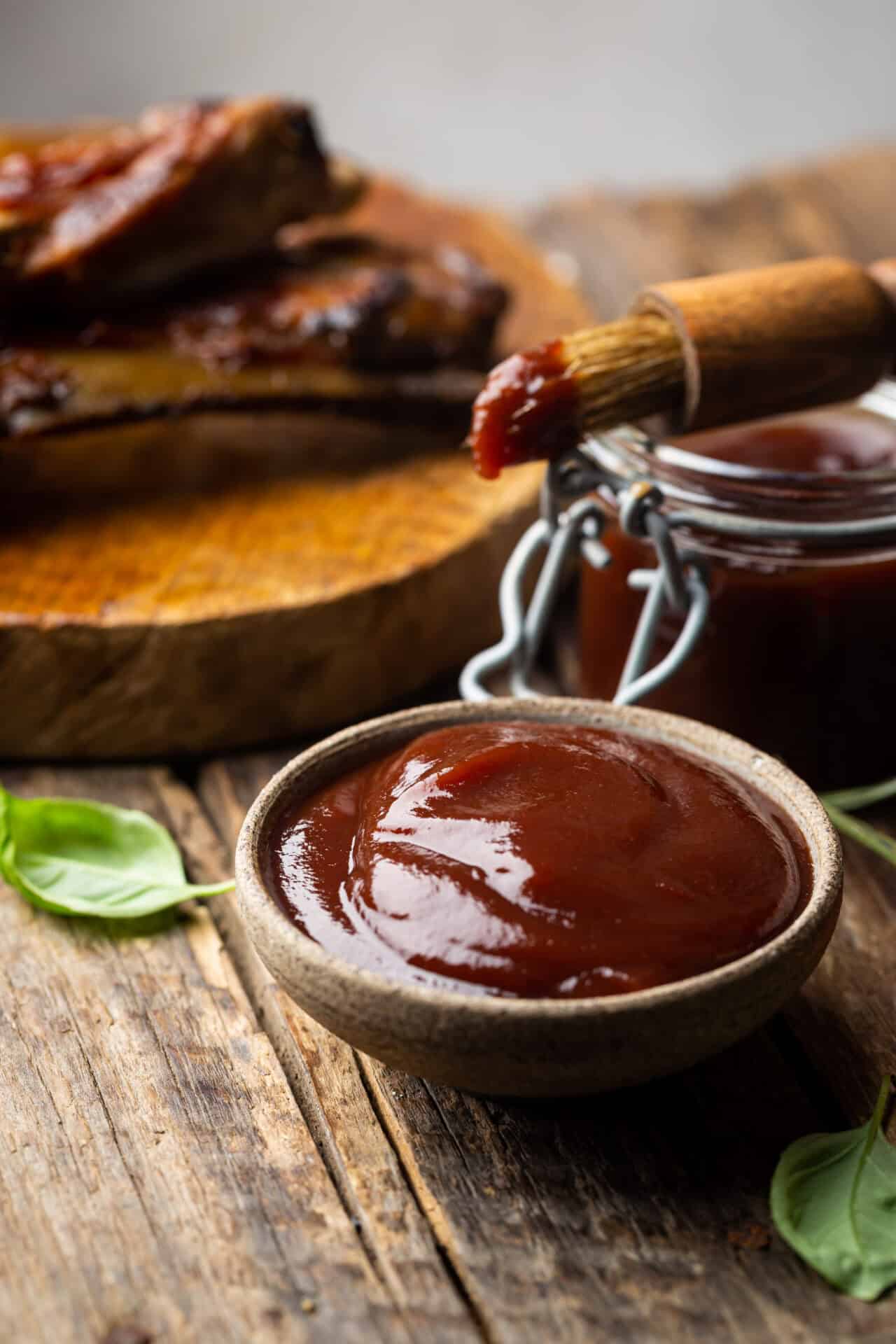 Barbecue sauce in a saucer with basting brush over rustic barn wood table with copy space.