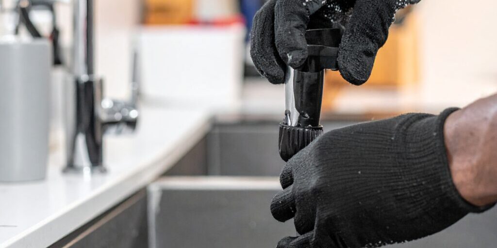 Firefly_Close-up of a plumber's gloved hands using a professional drain auger to clear a clog 541066