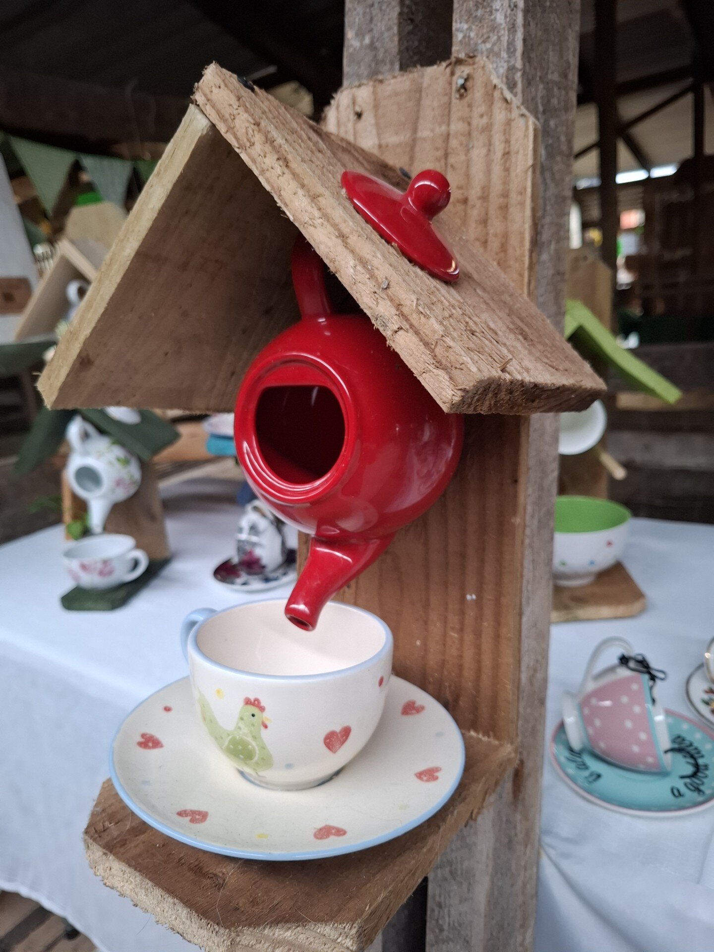 Upcycled wooden bird feeder with a red teapot design and a small cup for birdseed.
