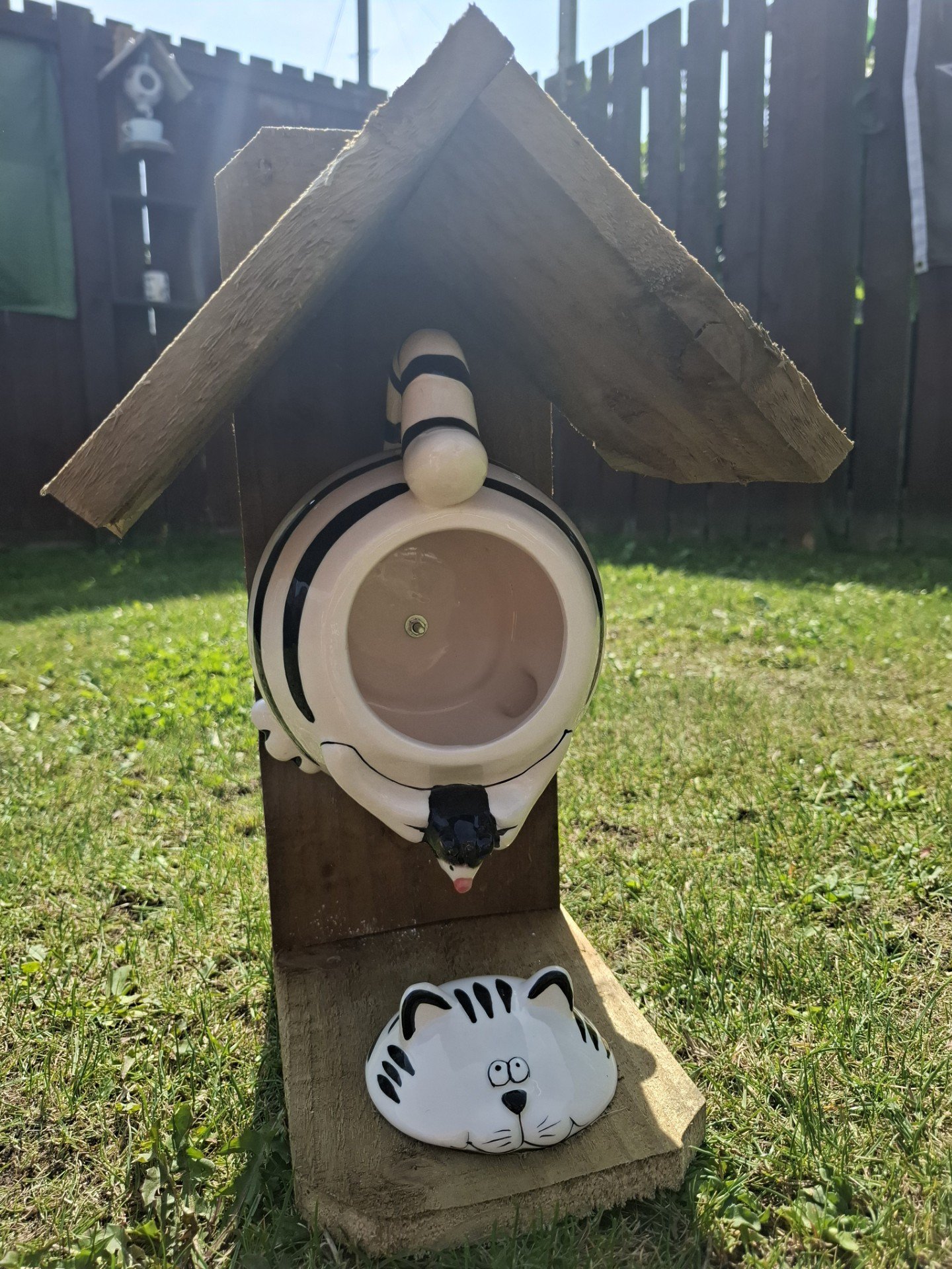 Upcycled wooden bird feeder with a zebra-shaped seed holder and roof in a garden setting.