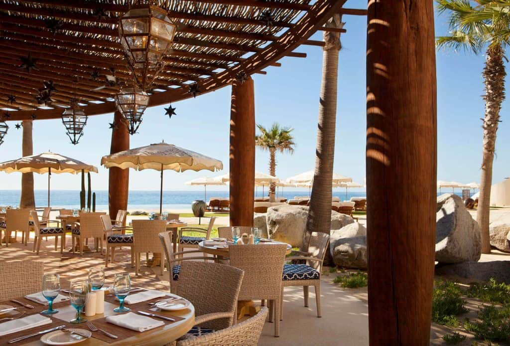 Pedregal Beachfront Restaurant Outdoor Dining Area With Ocean View And Shaded Seating, Tropical Palm Trees, And Elegant Table Setup For Luxury Dining At Pedregal.