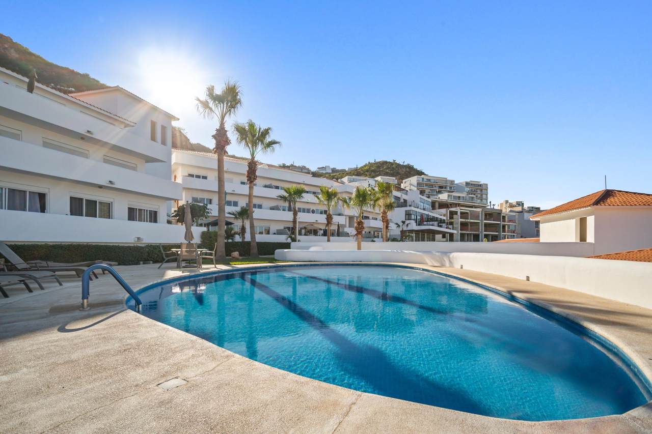 Camino El Colegio , #86 – Homes For Sale In Pedregal Luxury Pedregal Condo With Swimming Pool And Ocean Views, Modern White Buildings, Tall Palm Trees, And Hillside Background, In A Sunny Coastal Setting.