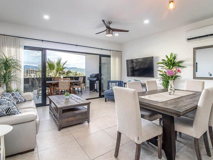 Modern Pedregal Condo Interior With Bright Living And Dining Areas, Large Sliding Doors To Balcony, Stylish Furnishings, And Scenic Mountain Views In The Background.