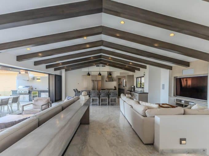 Spacious Pedregal Living Room With Vaulted Ceilings, Wooden Beams, Modern Decor, And Large Windows Overlooking A Outdoor Patio, Blending Comfort And Style In A Luxurious Home.