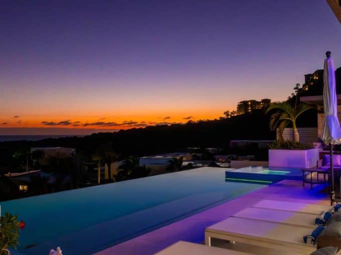 Stunning View Of Pedregal Luxury Estate With Infinity Pool At Sunset, Overlooking The Ocean And Rolling Hills, Featuring Modern Outdoor Furniture And Elegant Lighting For An Exclusive Coastal Retreat.