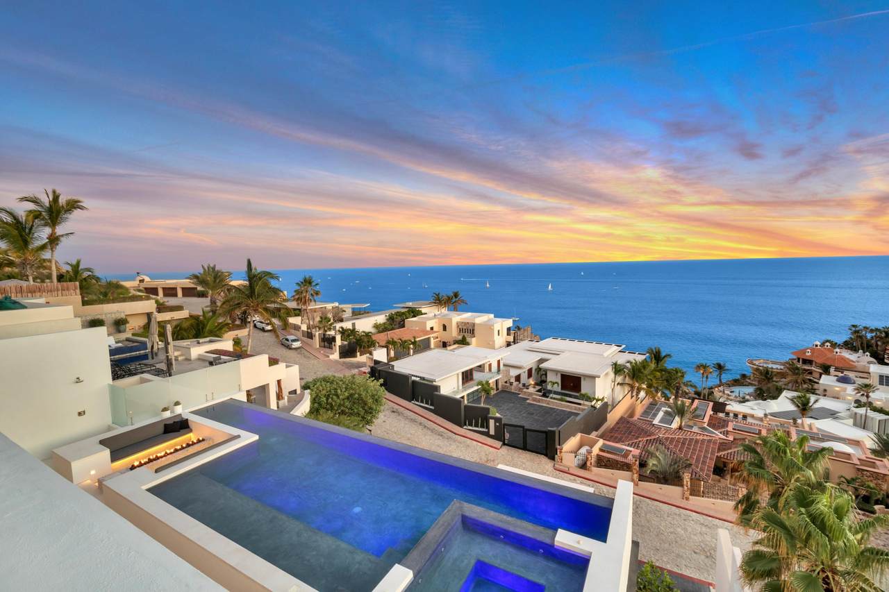 Stunning Pedregal Beachfront View Showcasing Luxury Homes, Infinity Pool, Lush Palm Trees, Vibrant Sunset, And Ocean Horizon, Perfect For Real Estate Investments And Exclusive Coastal Living.