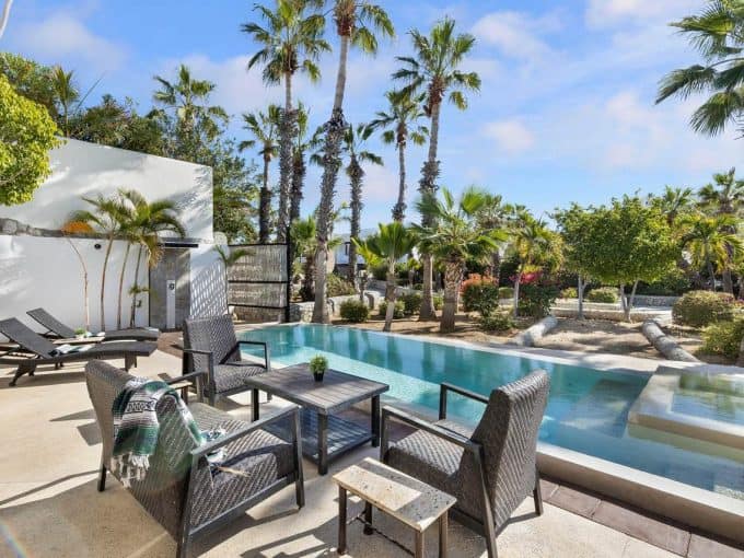 Luxurious Pedregal Backyard With Infinity Pool, Sun Loungers, Elegant Seating Area, Lush Palm Trees, And Vibrant Tropical Landscaping In A Tropical Paradise Setting.