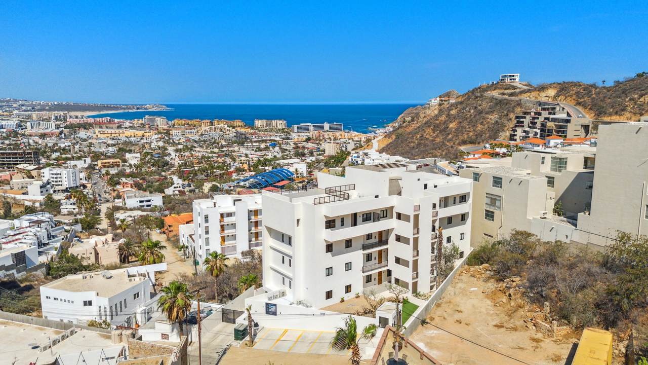 Modern Pedregal Residential Building With Ocean View And Hills In The Background, Featuring White Facades, Balconies, And Lush Landscaping, Offering Luxurious Living In The Vibrant Pedregal Neighborhood.