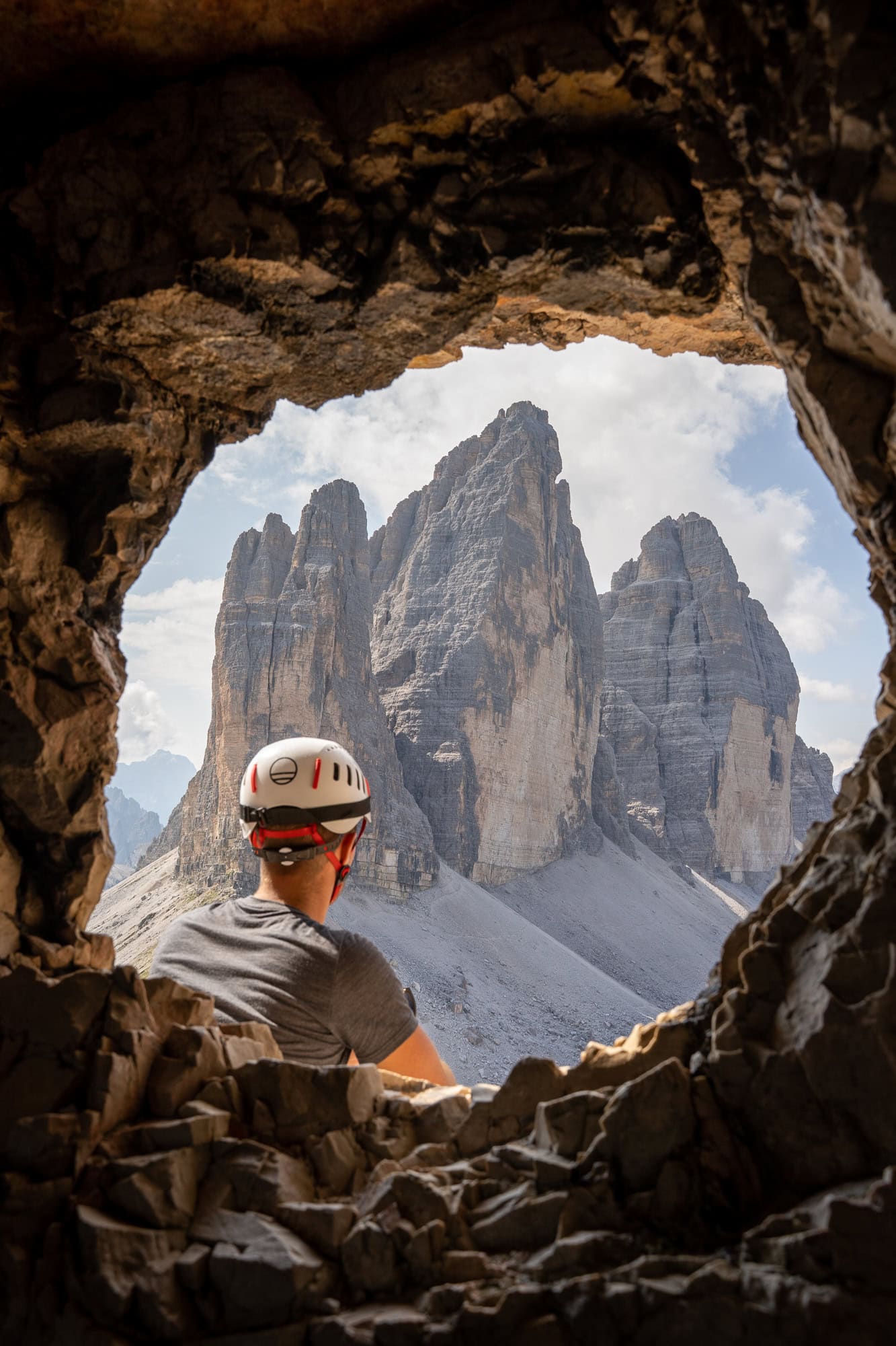 Rock opening with Tre Cime in the gap plus a person sitting in front of it, staring at the mountains