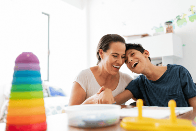 About 3 Deux personnes, une femme et un jeune homme, rient ensemble en jouant à un jeu de société avec des pièces colorées, illustrant la joie et l'interaction dans les soins