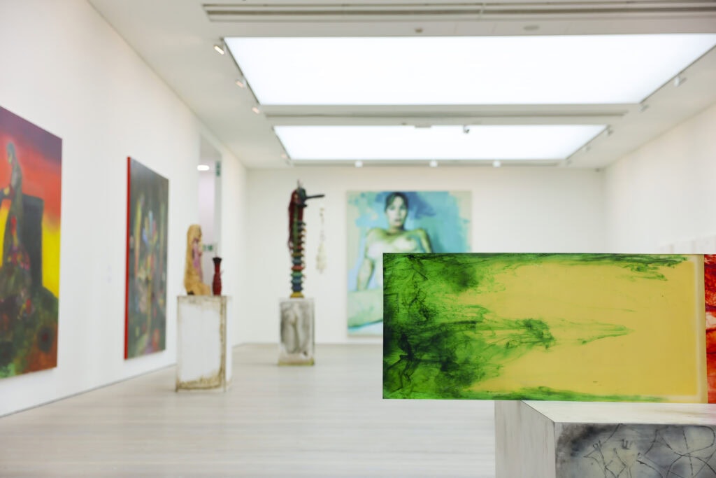 A contemporary art exhibition showcasing vibrant paintings and sculptures on display in a well-lit, minimalist gallery space.
