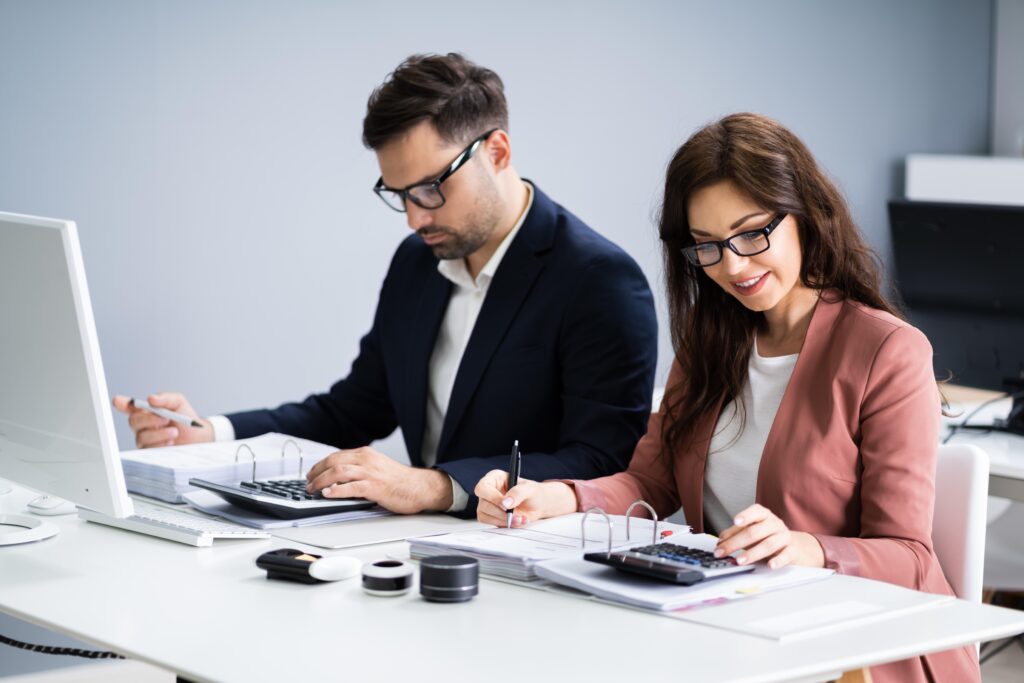 Business professionals working together at a desk with calculators and documents.