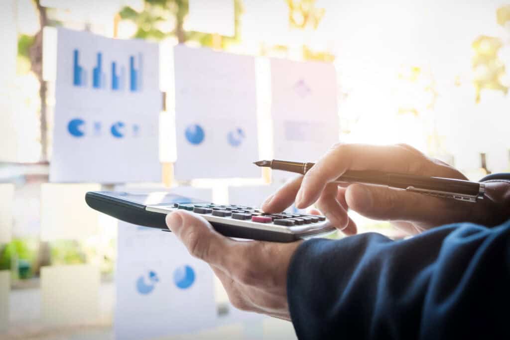 Person analyzing financial charts with calculator and graphs in background.