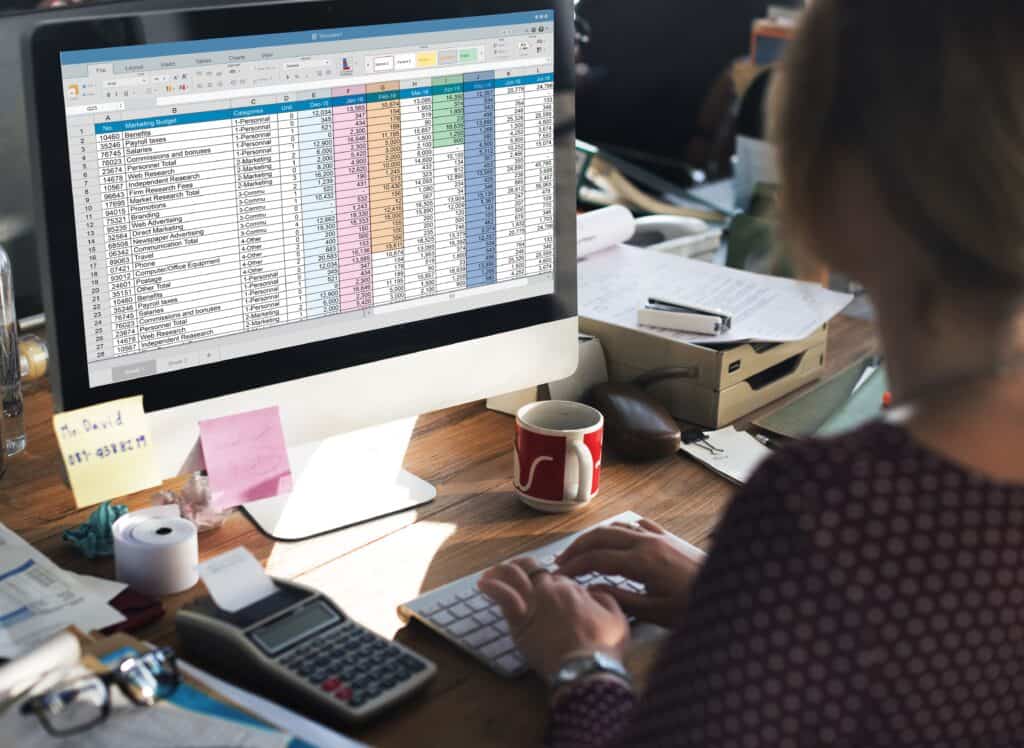 Person working on financial spreadsheet at office desk with computer and calculator.