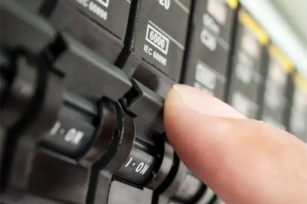 In Philadelphia, PA, a finger flips a switch on a black electrical circuit breaker labeled "6000," showcasing the precision of Circuit Breaker Installation in action.