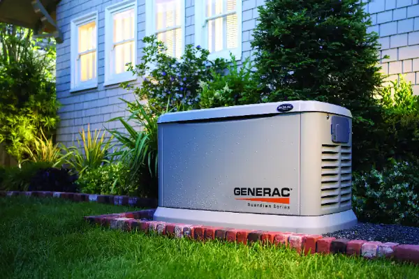 A Generac Guardian Series standby generator is installed outside a Philadelphia, PA home, surrounded by landscaping and sitting on a stone base after professional home generator installation.