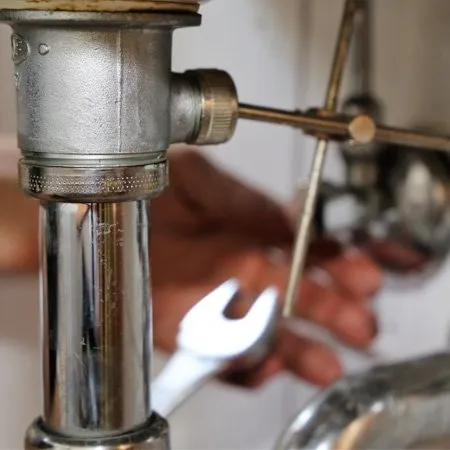 A close-up of a person’s hands using a wrench to adjust a metal pipe under a sink.