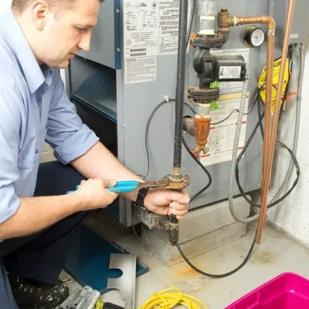 A technician uses a wrench to tighten a pipe connected to a furnace or boiler in a utility room.