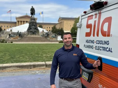 A man in a Sila uniform stands next to a Sila service van with a historic building and statue in the background.