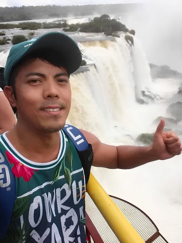 Traveler posing with a thumbs up in front of the powerful waterfalls of Iguazu Falls.