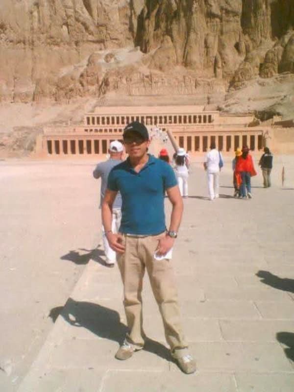 Traveler standing in front of the Temple of Hatshepsut in Luxor, Egypt, surrounded by towering sandstone cliffs.