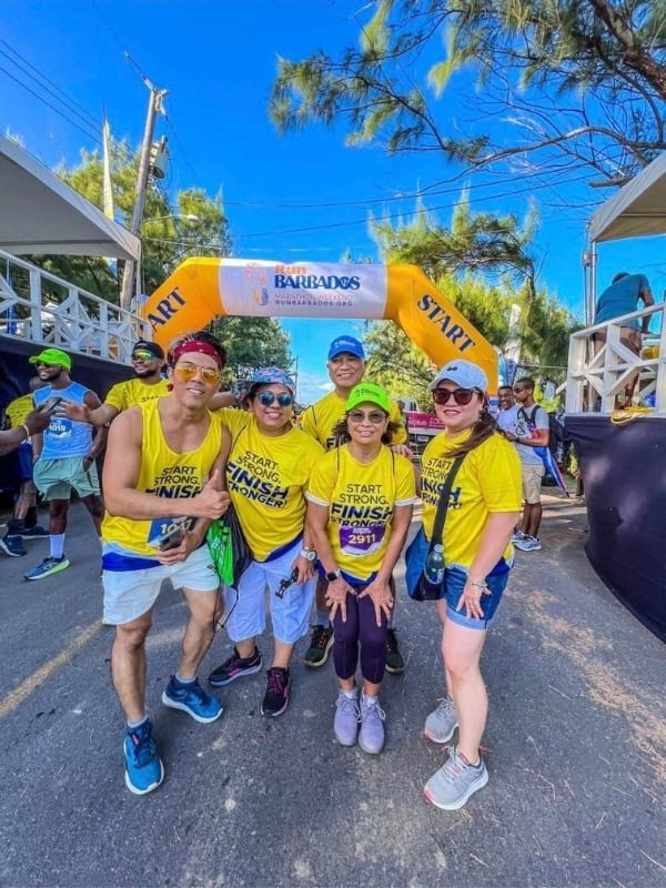 Group of runners wearing yellow Start Strong Finish Stronger shirts posing at the Barbados Marathon Weekend starting line.