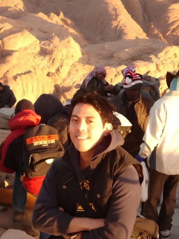 Traveler posing at Mount Sinai in Egypt among pilgrims and visitors against a rugged golden mountain landscape.